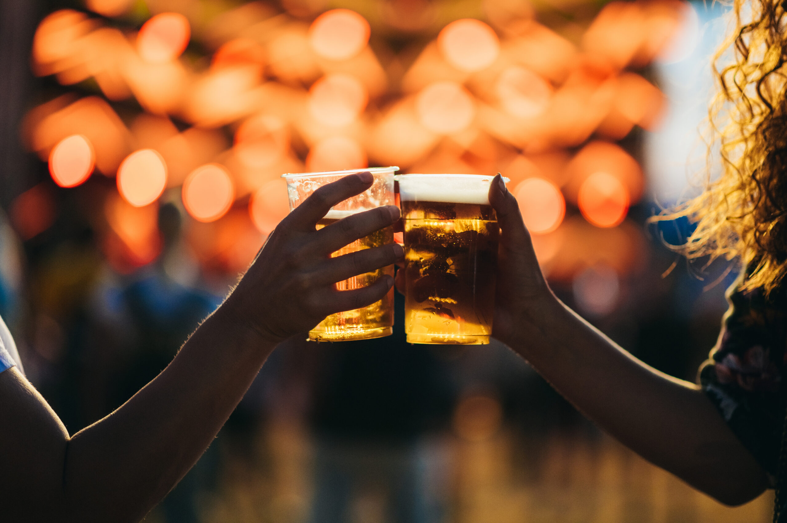 提灯の灯りを背に、ビールのカップを掲げて乾杯する2人