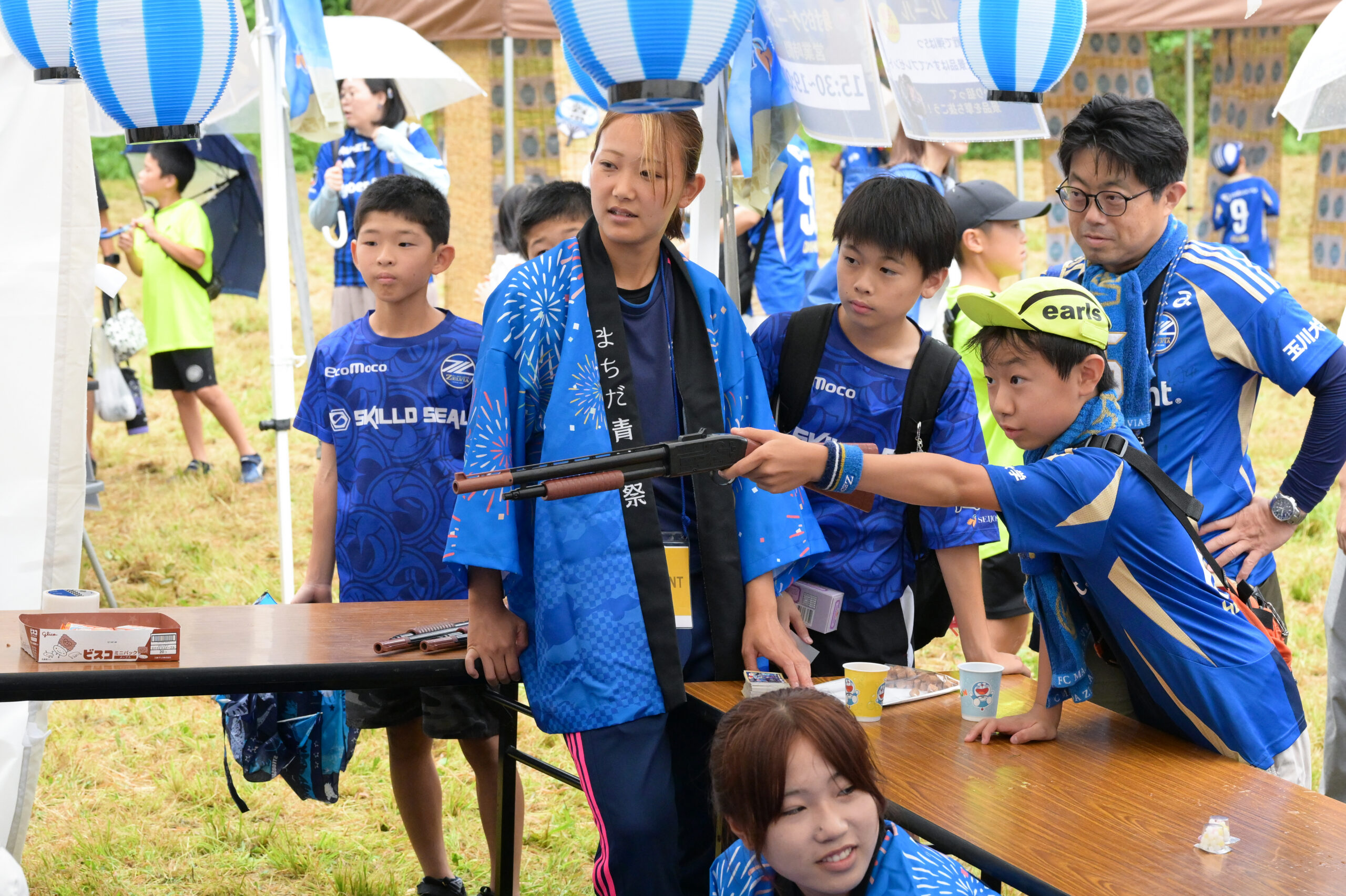 まちだ青城祭の縁日ブースで射的に挑戦する子どもと、法被姿のスタッフ